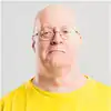 Senior man with glasses in a yellow shirt smiling outdoors.