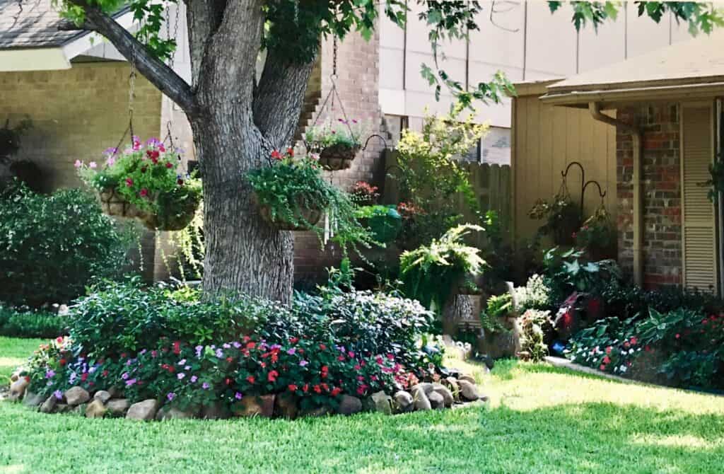 Lush garden with a large tree, colorful flowers, and well-kept lawn.